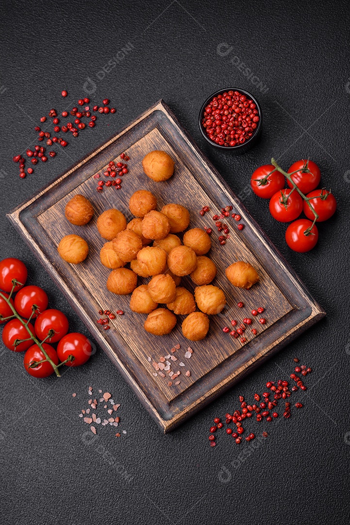 Deliciosas bolas de batata frita com mussarela à milanesa, sal, especiarias e ervas sobre um fundo escuro de concreto