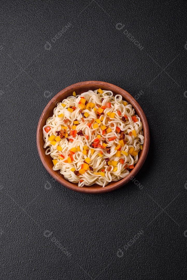 Delicioso macarrão asiático fresco com pedaços de legumes, carne, com sal, especiarias e ervas sobre um fundo escuro de concreto