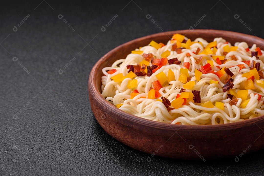 Delicioso macarrão asiático fresco com pedaços de legumes, carne, com sal, especiarias e ervas sobre um fundo escuro de concreto