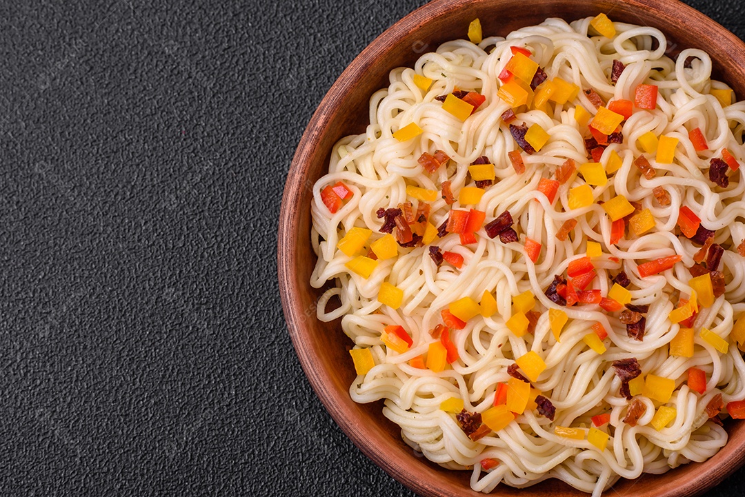 Delicioso macarrão asiático fresco com pedaços de legumes, carne, com sal, especiarias e ervas sobre um fundo escuro de concreto