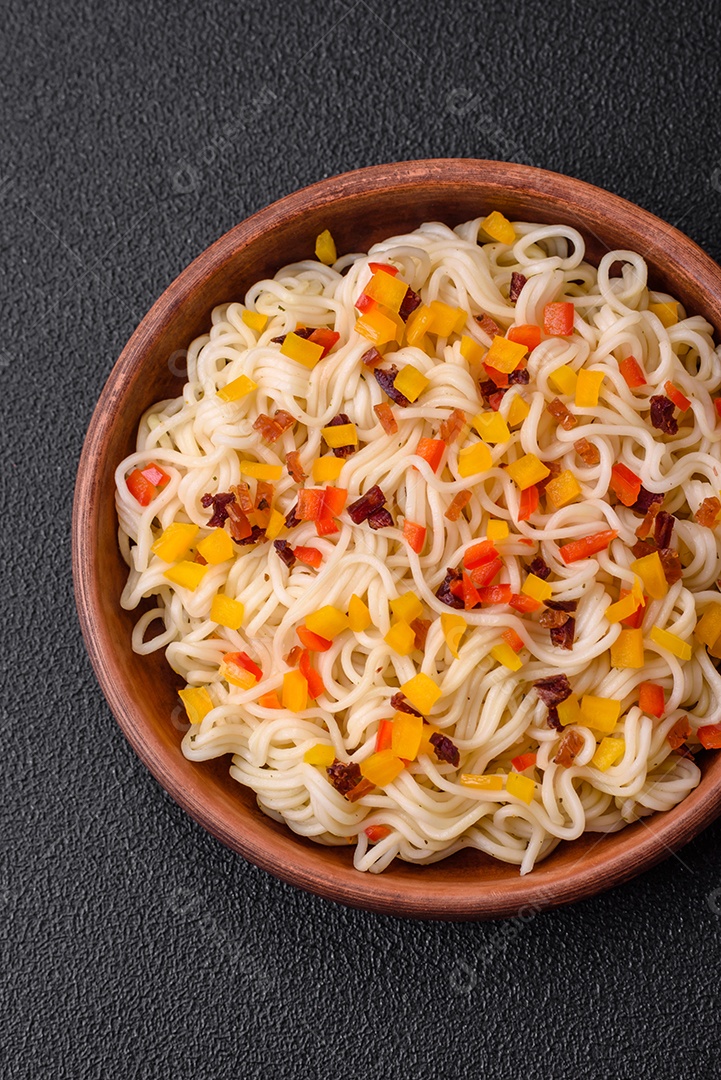 Delicioso macarrão asiático fresco com pedaços de legumes, carne, com sal, especiarias e ervas sobre um fundo escuro de concreto