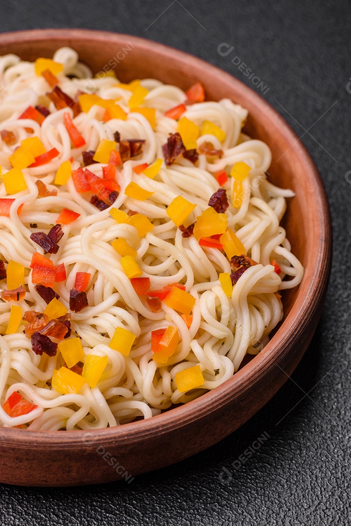 Delicioso macarrão asiático fresco com pedaços de legumes, carne, com sal, especiarias e ervas sobre um fundo escuro de concreto