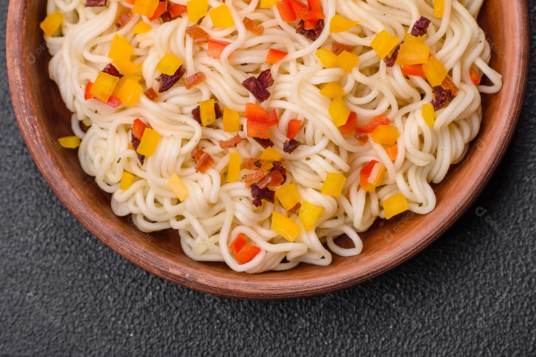 Delicioso macarrão asiático fresco com pedaços de legumes, carne, com sal, especiarias e ervas sobre um fundo escuro de concreto