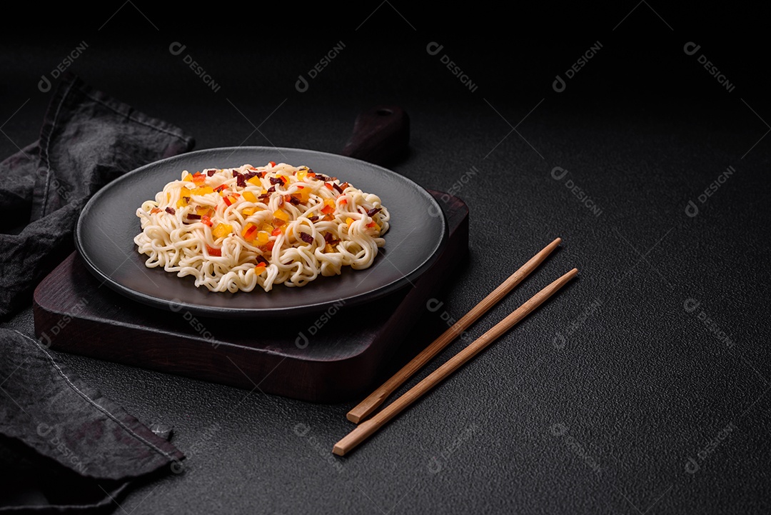 Delicioso macarrão asiático fresco com pedaços de legumes, carne, com sal, especiarias e ervas sobre um fundo escuro de concreto