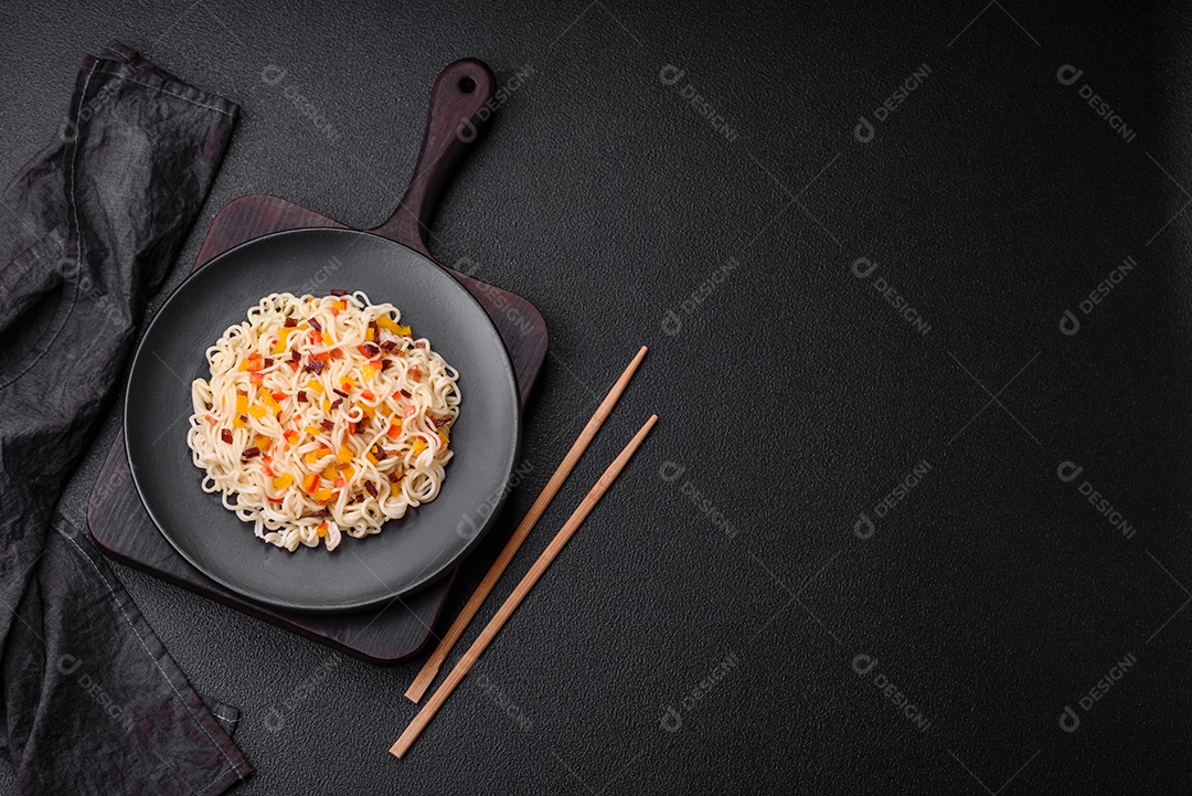 Delicioso macarrão asiático fresco com pedaços de legumes, carne, com sal, especiarias e ervas sobre um fundo escuro de concreto