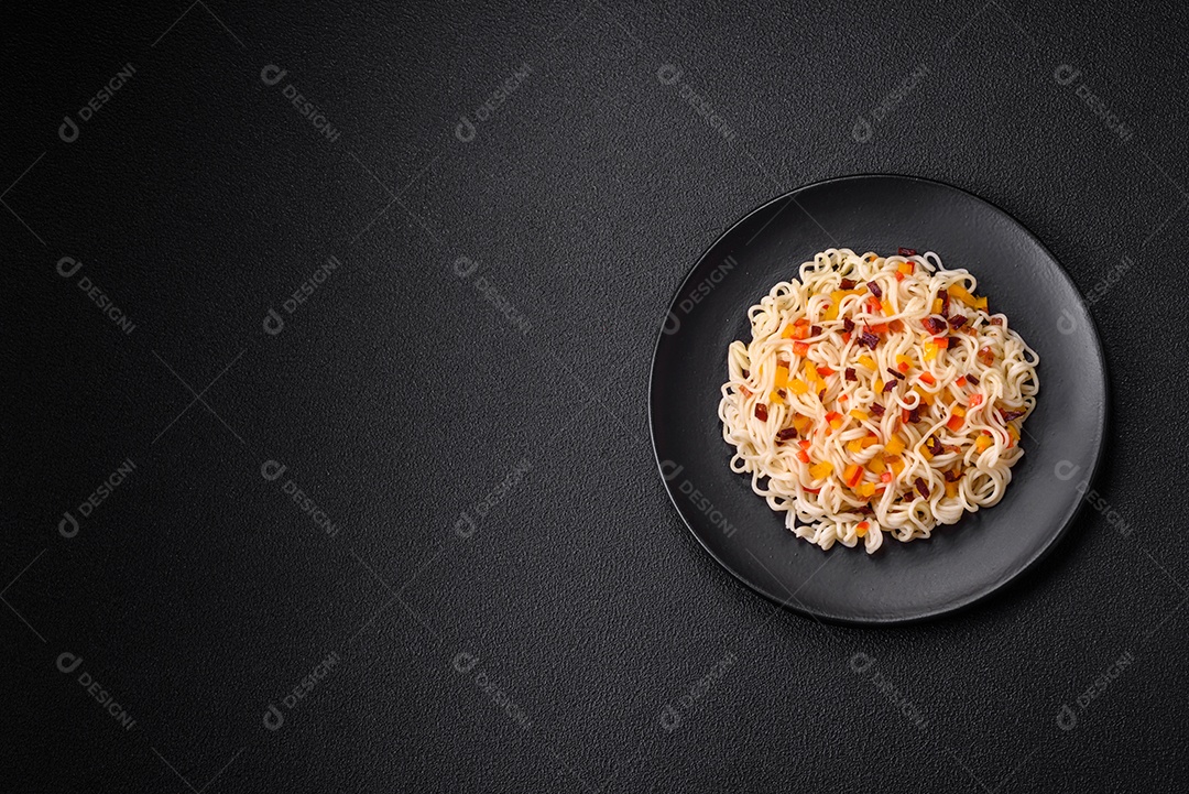 Delicioso macarrão asiático fresco com pedaços de legumes, carne, com sal, especiarias e ervas sobre um fundo escuro de concreto