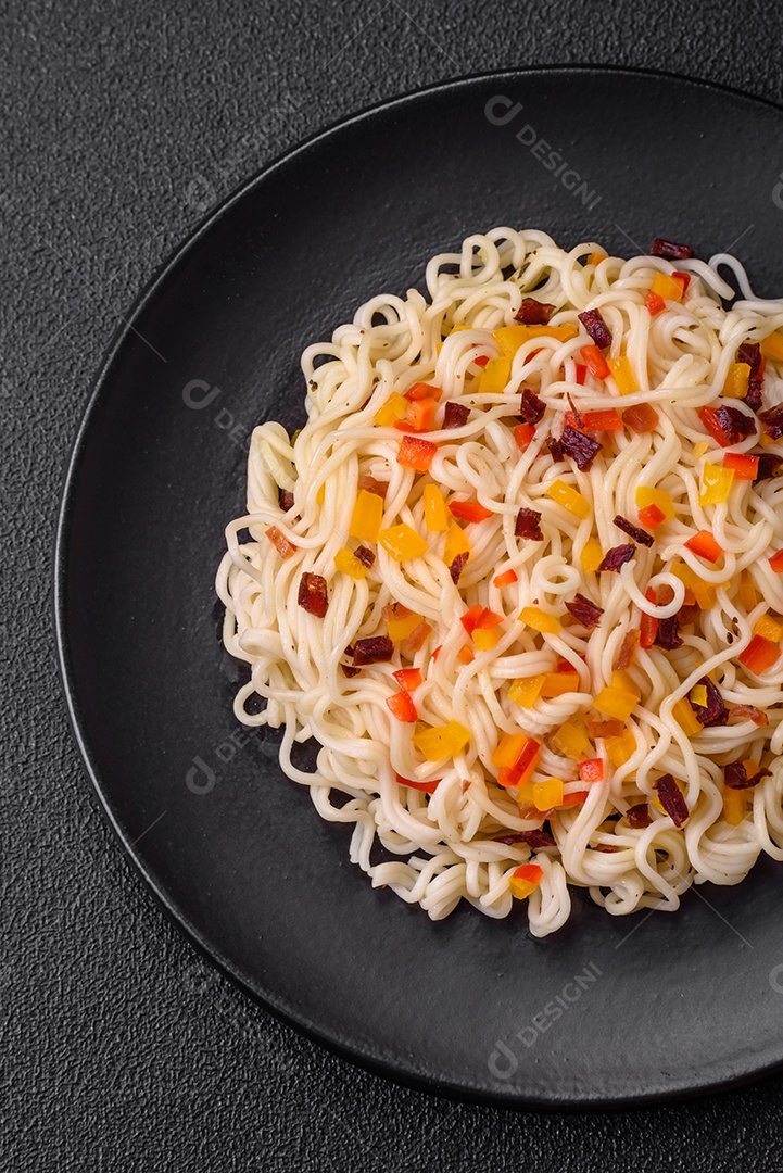 Delicioso macarrão asiático fresco com pedaços de legumes, carne, com sal, especiarias e ervas sobre um fundo escuro de concreto