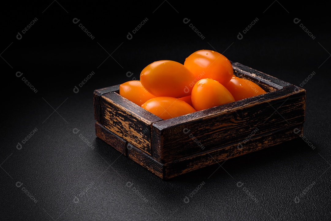 Tomates amarelos frescos e brilhantes em forma de ameixa sobre um fundo de concreto texturizado preto