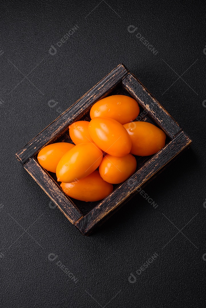 Tomates amarelos frescos e brilhantes em forma de ameixa sobre um fundo de concreto texturizado preto
