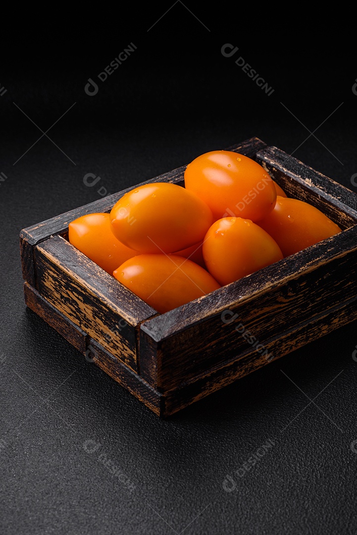 Tomates amarelos frescos e brilhantes em forma de ameixa sobre um fundo de concreto texturizado preto