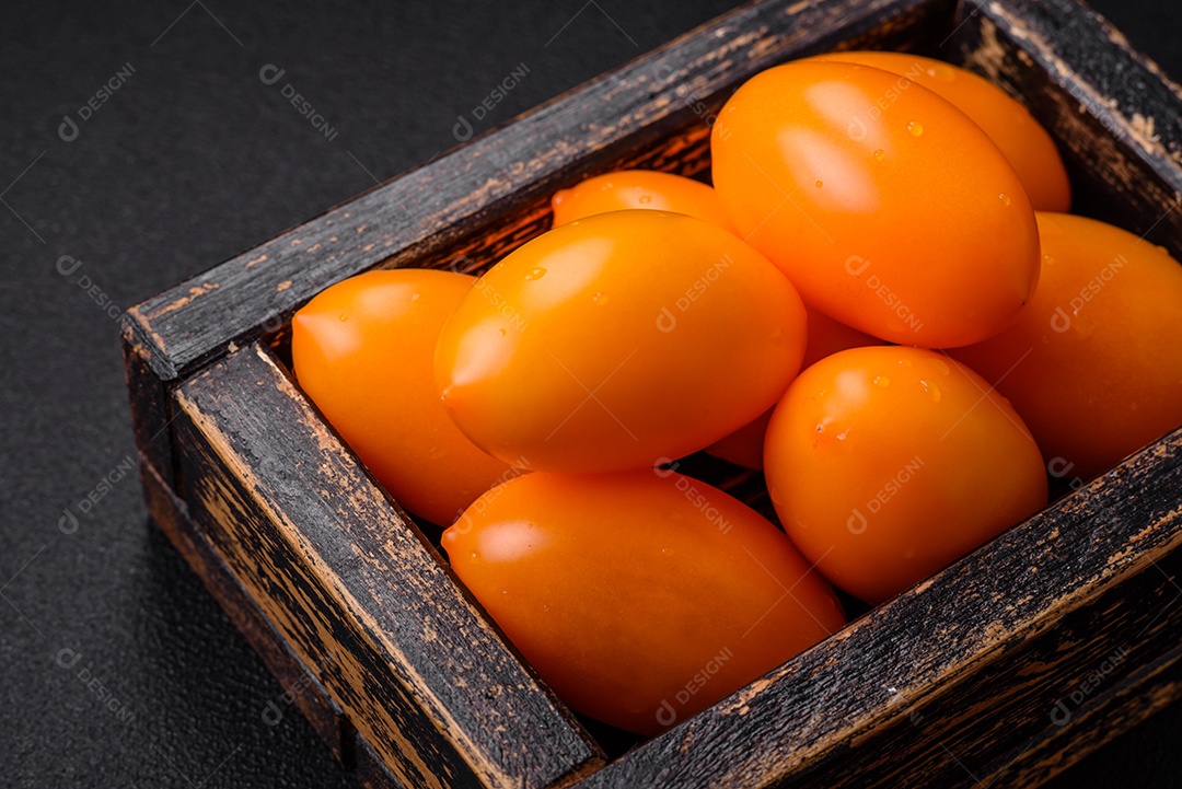 Tomates amarelos frescos e brilhantes em forma de ameixa sobre um fundo de concreto texturizado preto