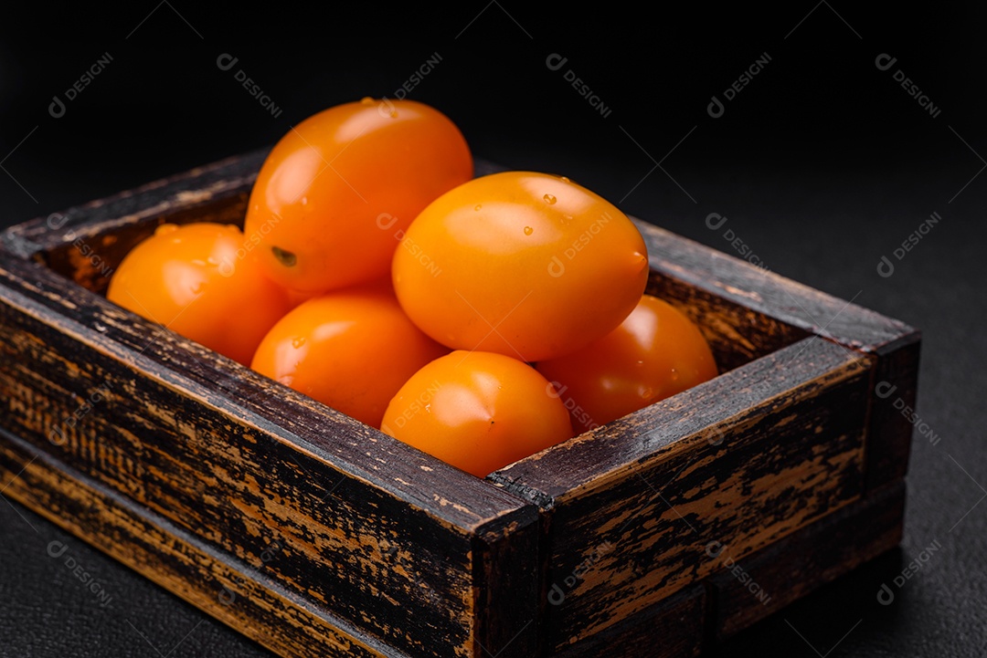Tomates amarelos frescos e brilhantes em forma de ameixa sobre um fundo de concreto texturizado preto