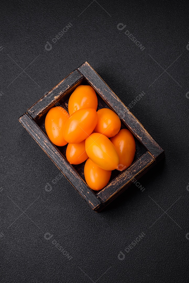 Tomates amarelos frescos e brilhantes em forma de ameixa sobre um fundo de concreto texturizado preto