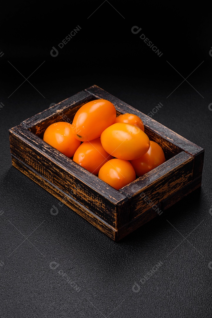 Tomates amarelos frescos e brilhantes em forma de ameixa sobre um fundo de concreto texturizado preto