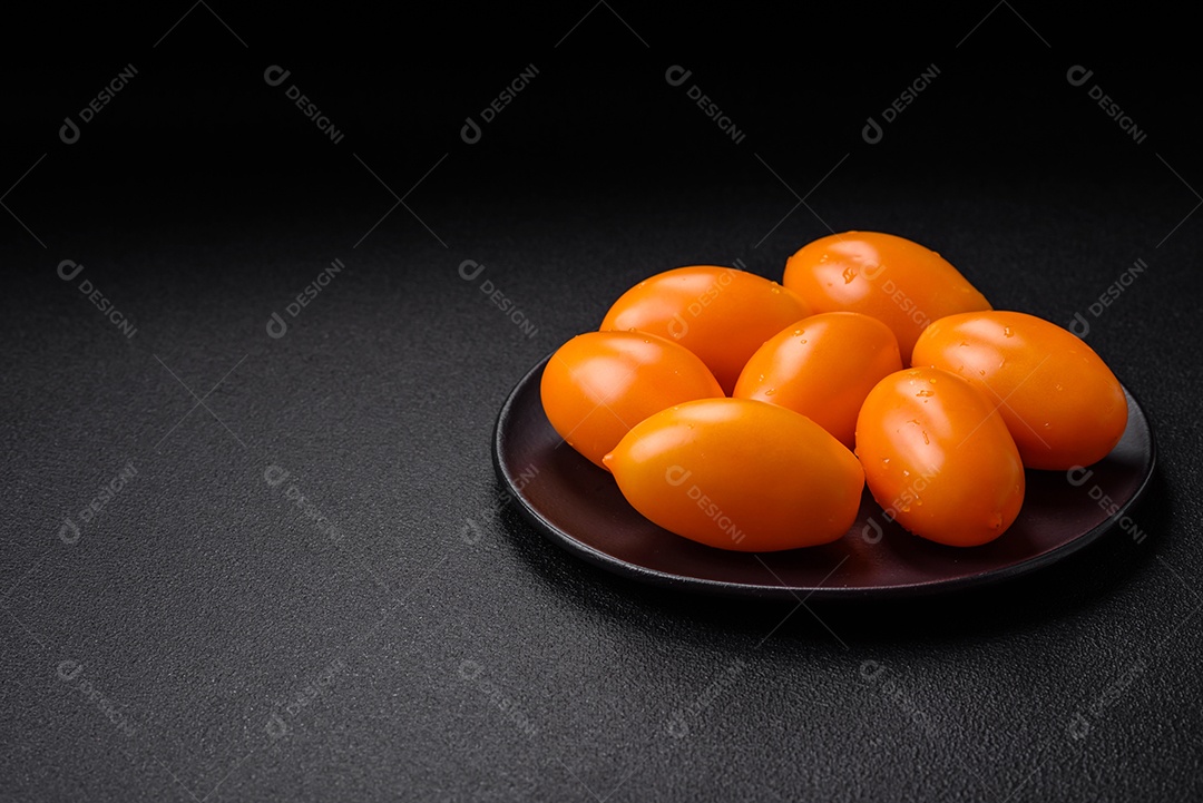 Tomates amarelos frescos e brilhantes em forma de ameixa sobre um fundo de concreto texturizado preto