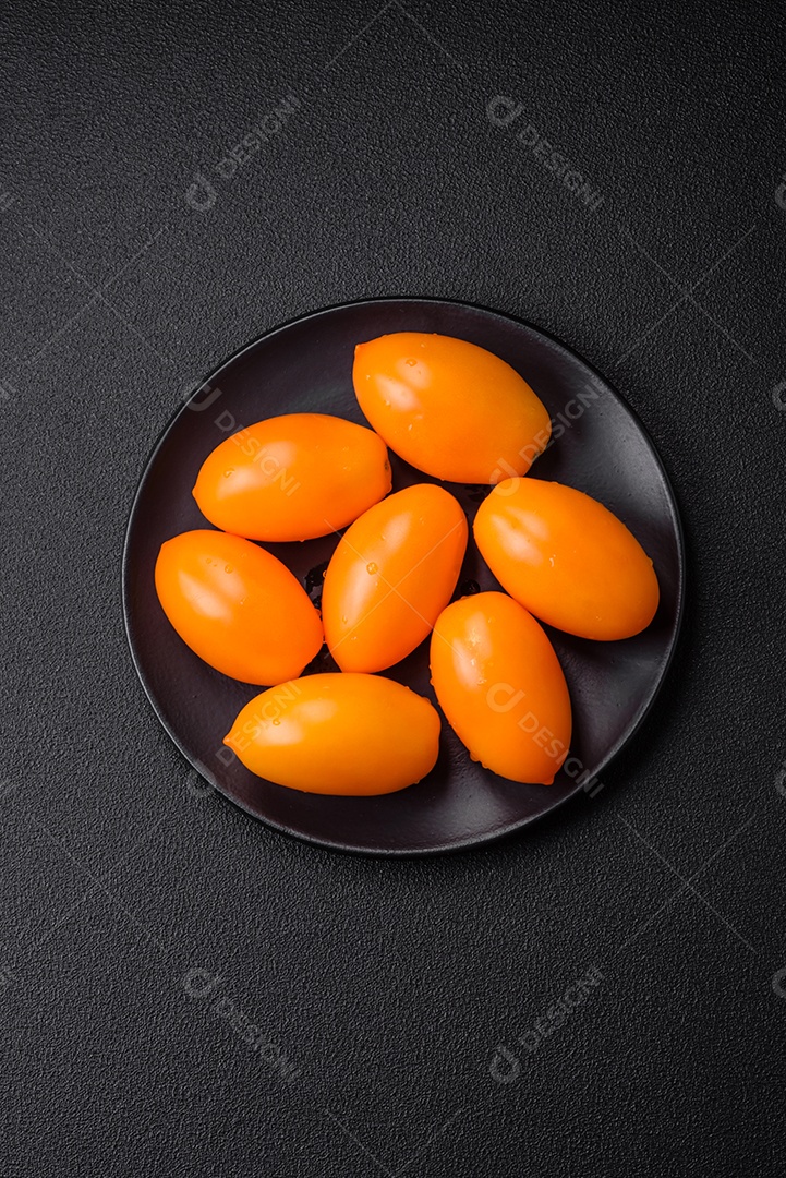 Tomates amarelos frescos e brilhantes em forma de ameixa sobre um fundo de concreto texturizado preto