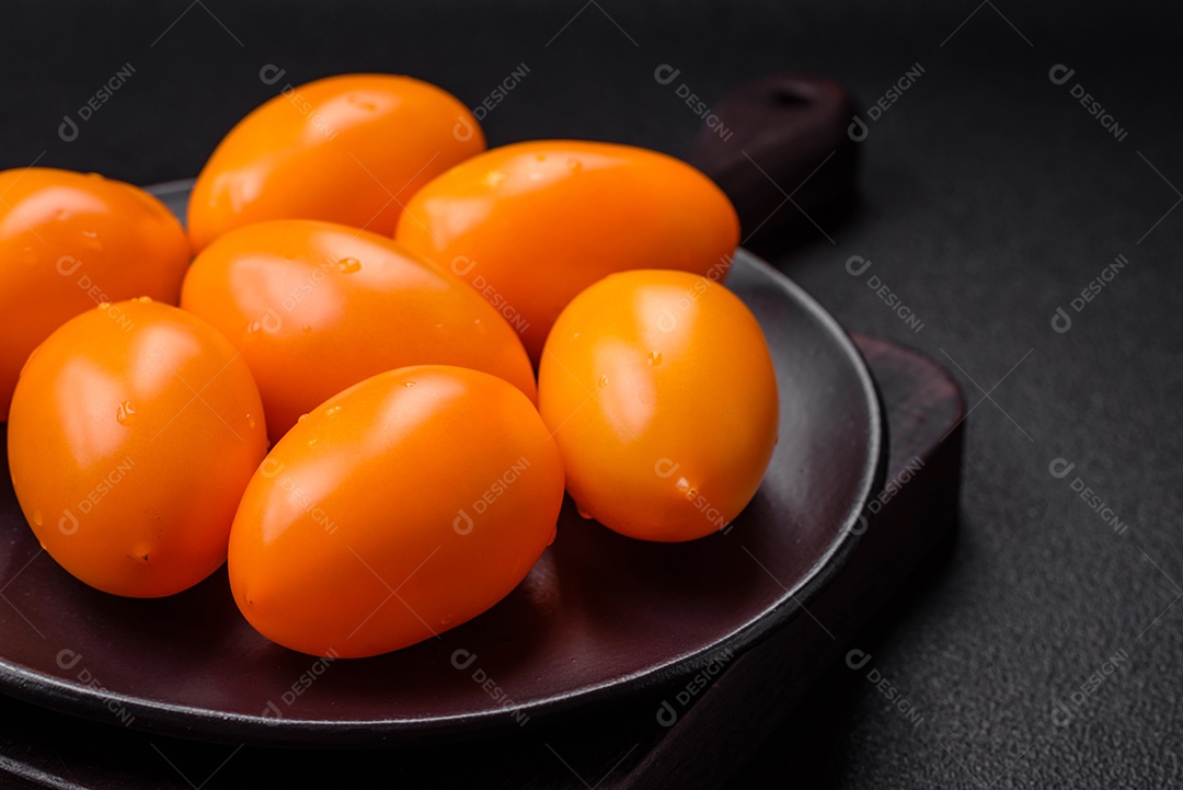 Tomates amarelos frescos e brilhantes em forma de ameixa sobre um fundo de concreto texturizado preto