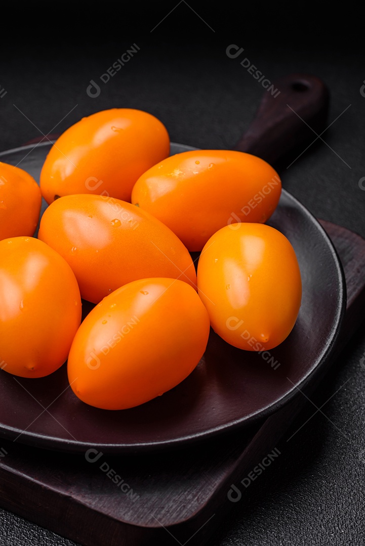 Tomates amarelos frescos e brilhantes em forma de ameixa sobre um fundo de concreto texturizado preto