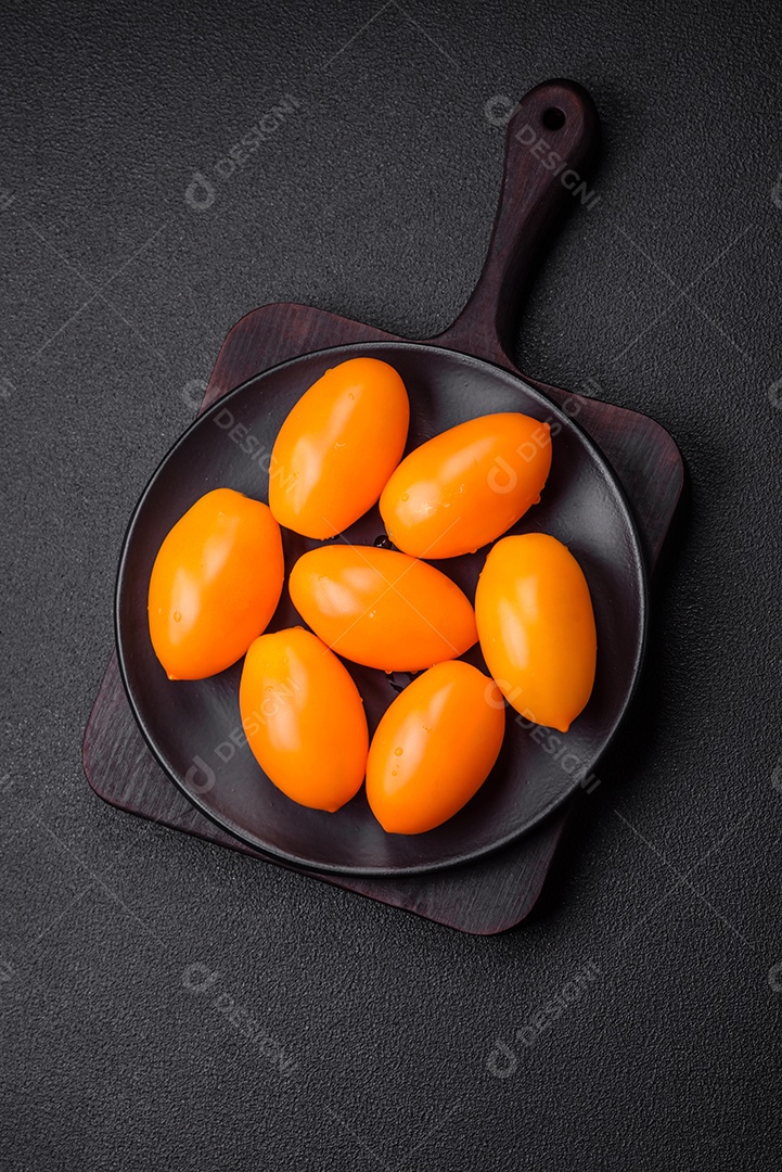 Tomates amarelos frescos e brilhantes em forma de ameixa sobre um fundo de concreto texturizado preto