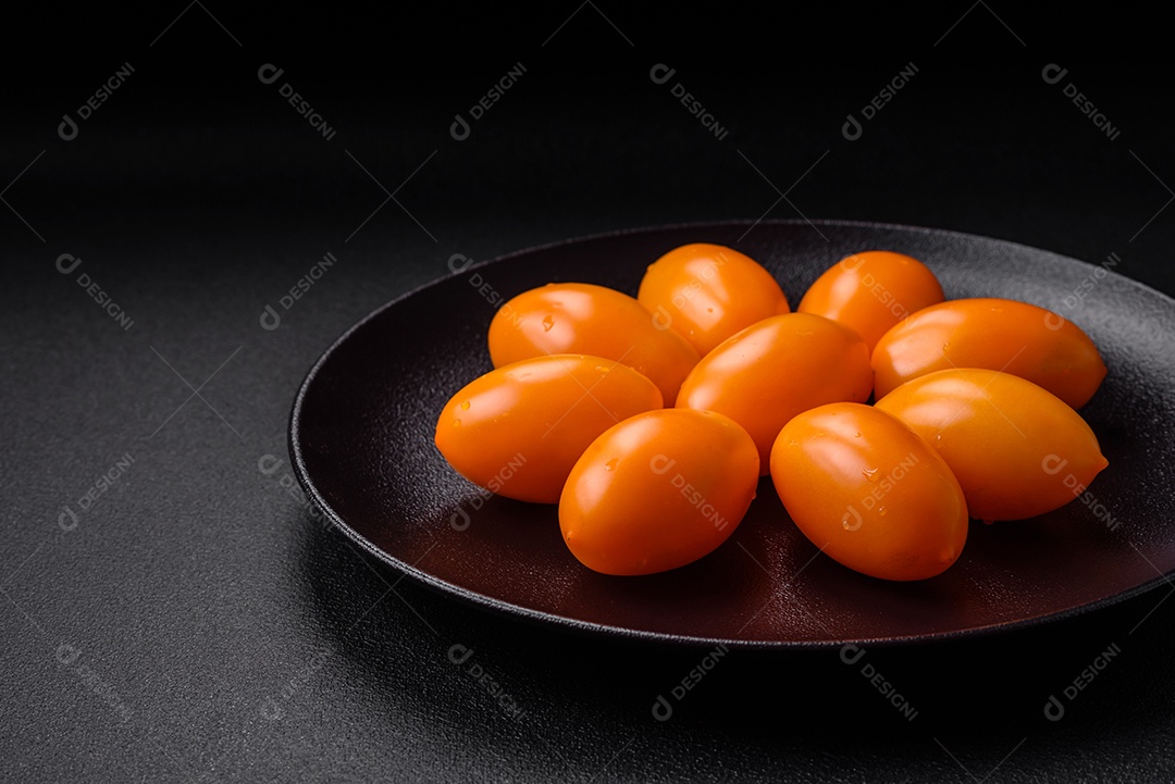 Tomates amarelos frescos e brilhantes em forma de ameixa sobre um fundo de concreto texturizado preto