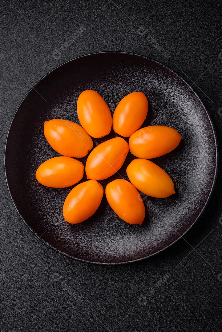 Tomates amarelos frescos e brilhantes em forma de ameixa sobre um fundo de concreto texturizado preto