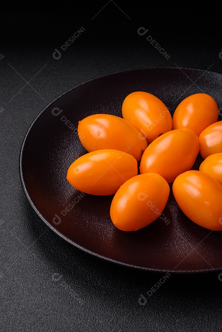 Tomates amarelos frescos e brilhantes em forma de ameixa sobre um fundo de concreto texturizado preto