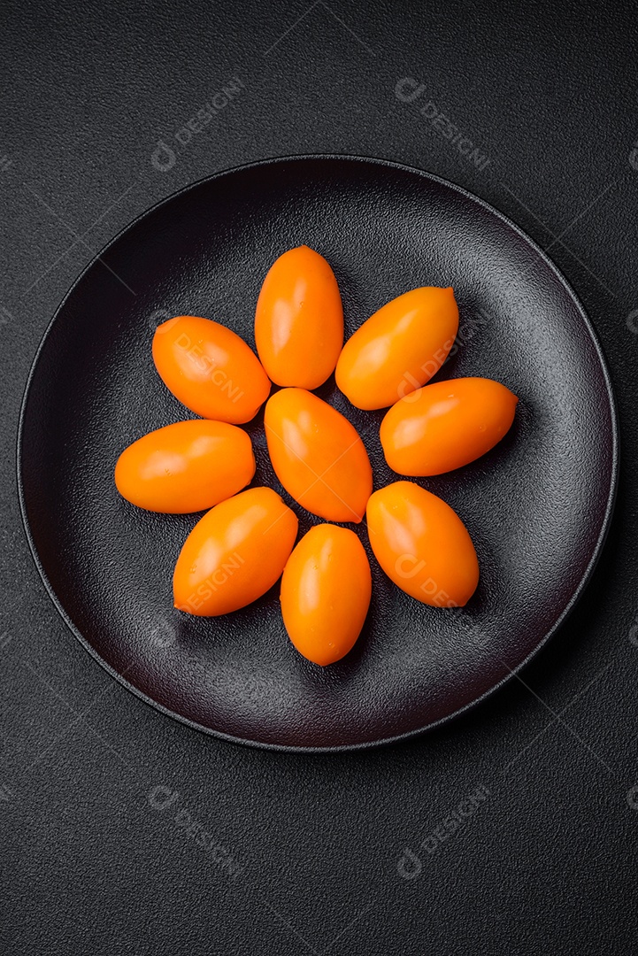 Tomates amarelos frescos e brilhantes em forma de ameixa sobre um fundo de concreto texturizado preto