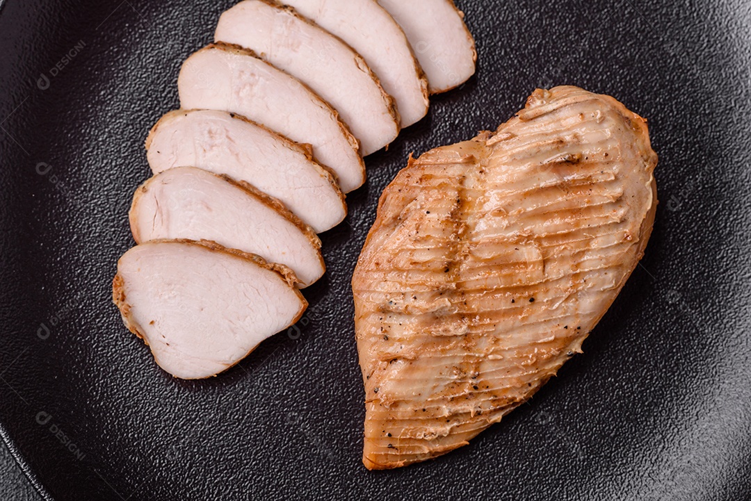 Delicioso suculento filé de frango grelhado com sal, especiarias e ervas sobre um fundo escuro de concreto