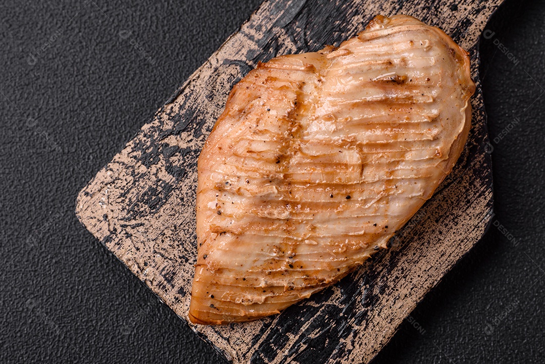 Delicioso suculento filé de frango grelhado com sal, especiarias e ervas sobre um fundo escuro de concreto