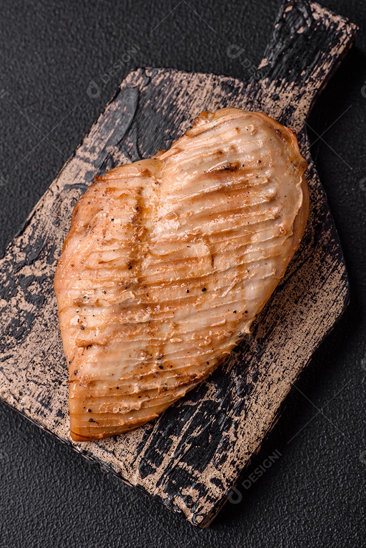 Delicioso suculento filé de frango grelhado com sal, especiarias e ervas sobre um fundo escuro de concreto