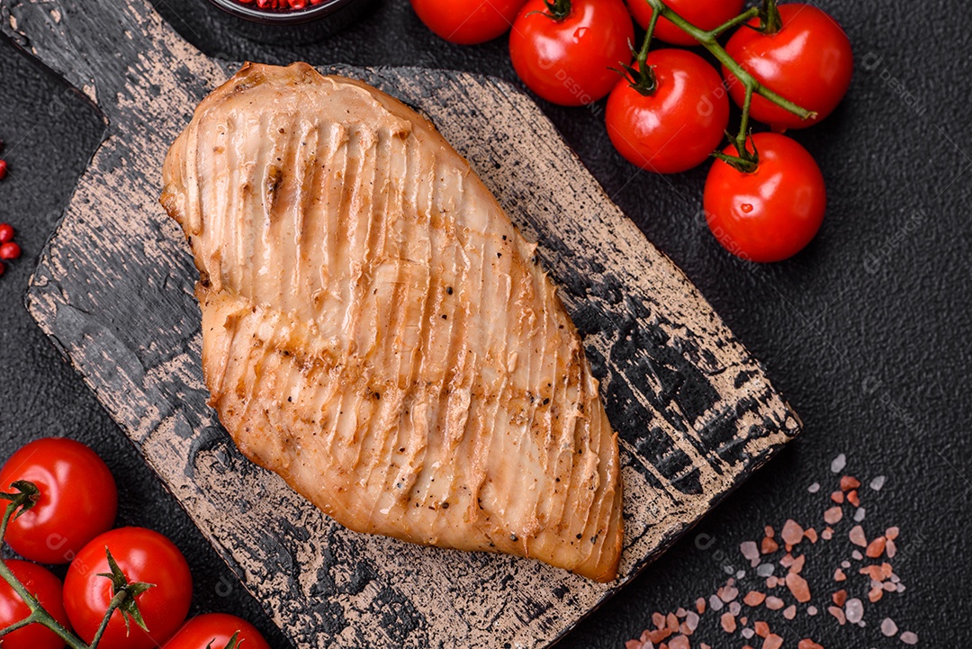 Delicioso suculento filé de frango grelhado com sal, especiarias e ervas sobre um fundo escuro de concreto