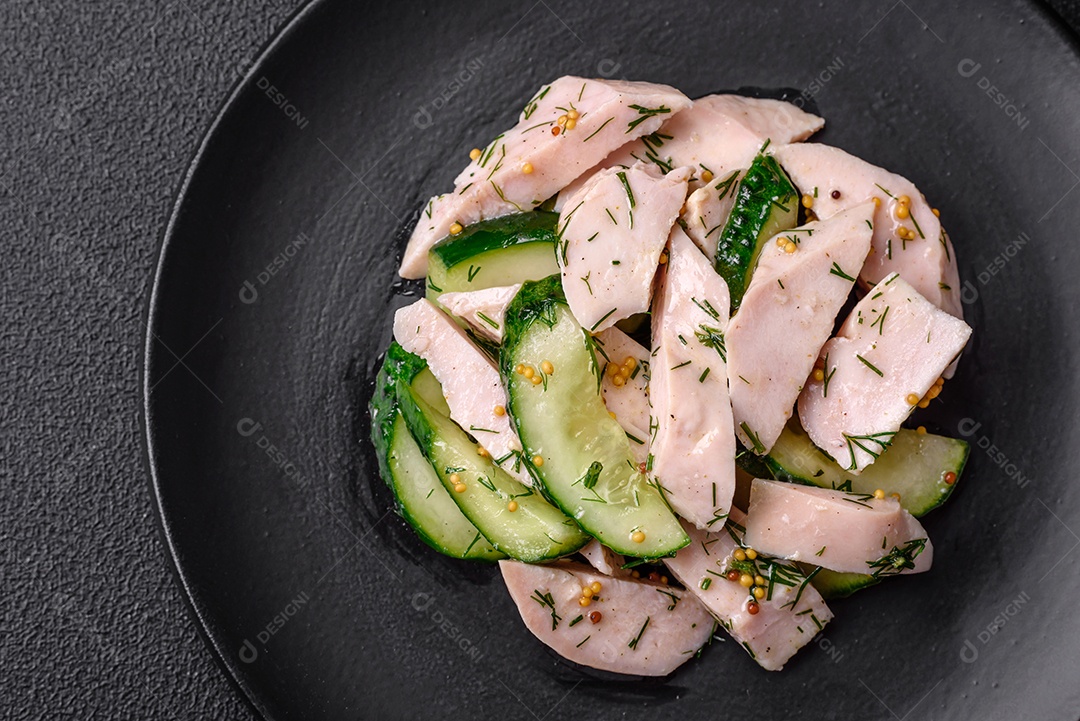 Deliciosa salada fresca e suculenta de pepino e fatias de frango grelhado, com mostarda francesa, sal e especiarias sobre um fundo escuro de concreto