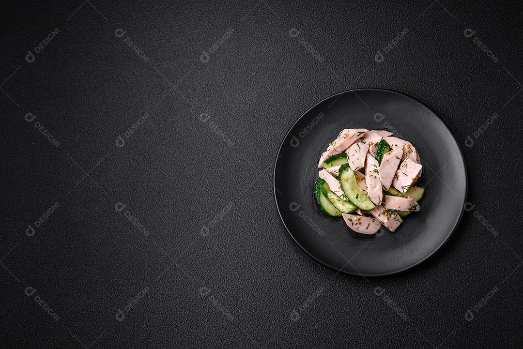 Deliciosa salada fresca e suculenta de pepino e fatias de frango grelhado, com mostarda francesa, sal e especiarias sobre um fundo escuro de concreto