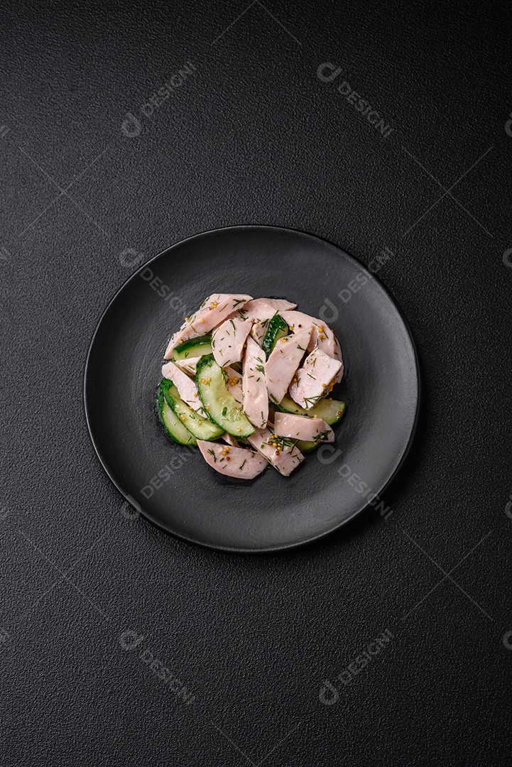 Deliciosa salada fresca e suculenta de pepino e fatias de frango grelhado, com mostarda francesa, sal e especiarias sobre um fundo escuro de concreto