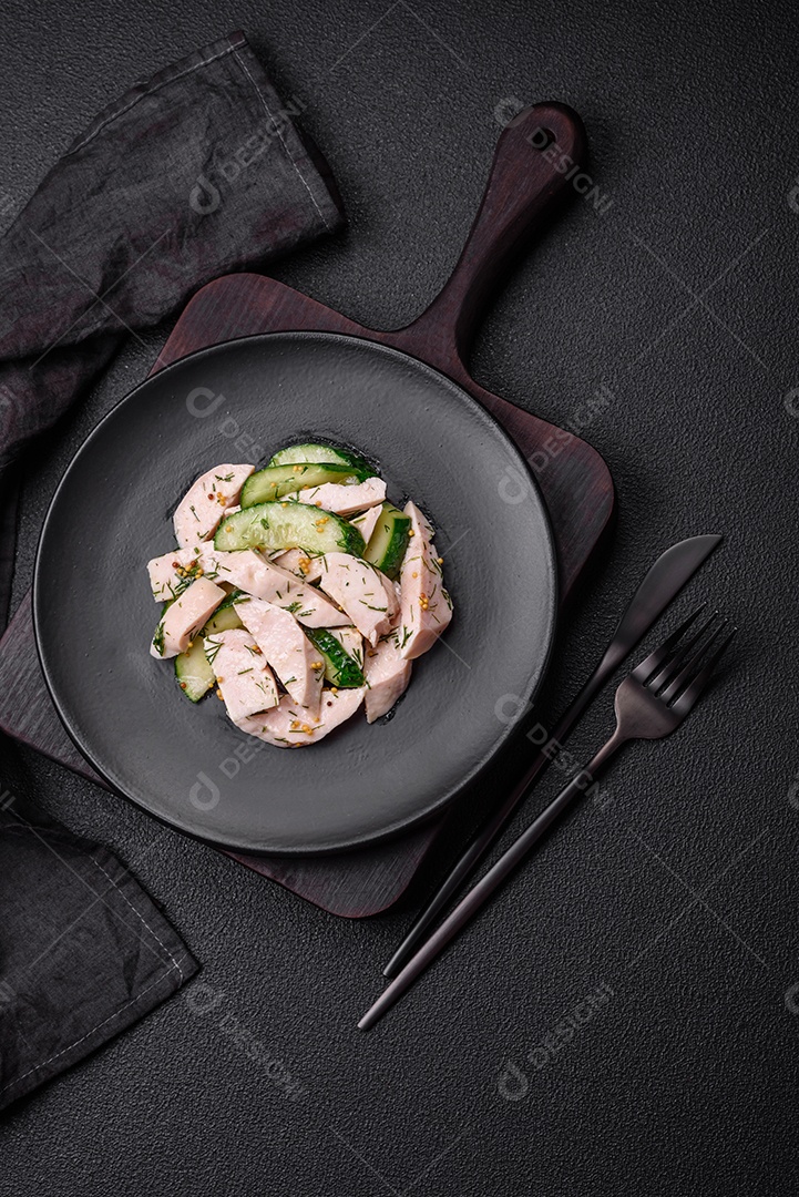 Deliciosa salada fresca e suculenta de pepino e fatias de frango grelhado, com mostarda francesa, sal e especiarias sobre um fundo escuro de concreto
