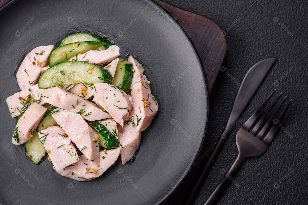 Deliciosa salada fresca e suculenta de pepino e fatias de frango grelhado, com mostarda francesa, sal e especiarias sobre um fundo escuro de concreto