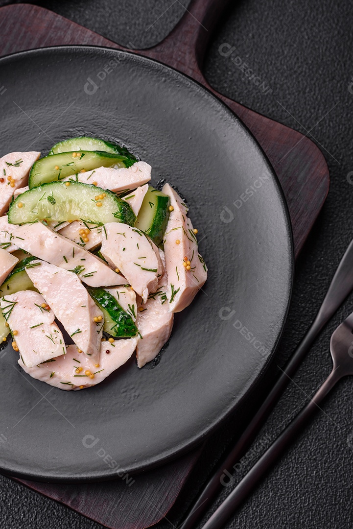 Deliciosa salada fresca e suculenta de pepino e fatias de frango grelhado, com mostarda francesa, sal e especiarias sobre um fundo escuro de concreto