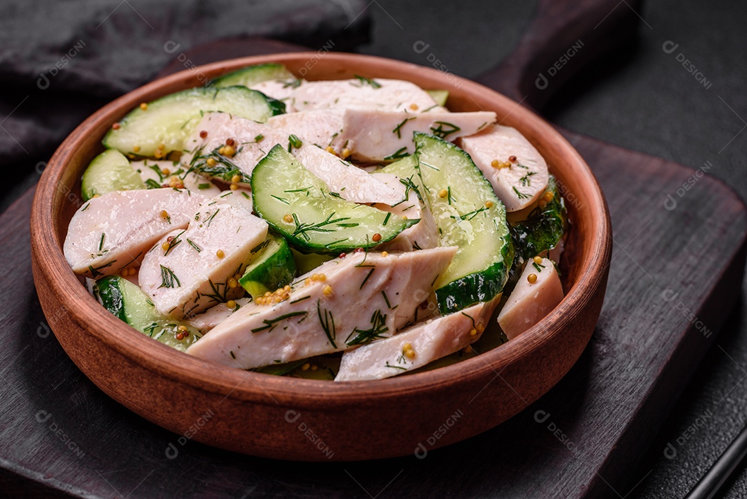 Deliciosa salada fresca e suculenta de pepino e fatias de frango grelhado, com mostarda francesa, sal e especiarias sobre um fundo escuro de concreto