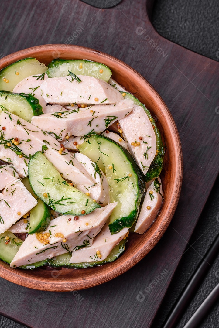 Deliciosa salada fresca e suculenta de pepino e fatias de frango grelhado, com mostarda francesa, sal e especiarias sobre um fundo escuro de concreto