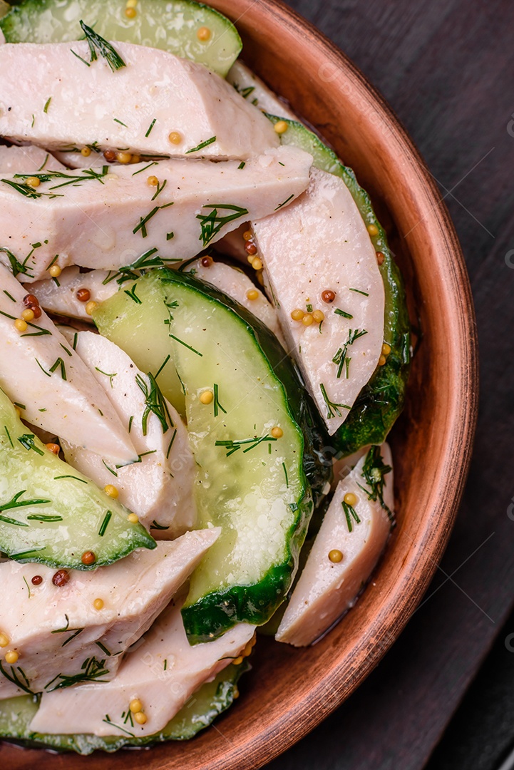 Deliciosa salada fresca e suculenta de pepino e fatias de frango grelhado, com mostarda francesa, sal e especiarias sobre um fundo escuro de concreto