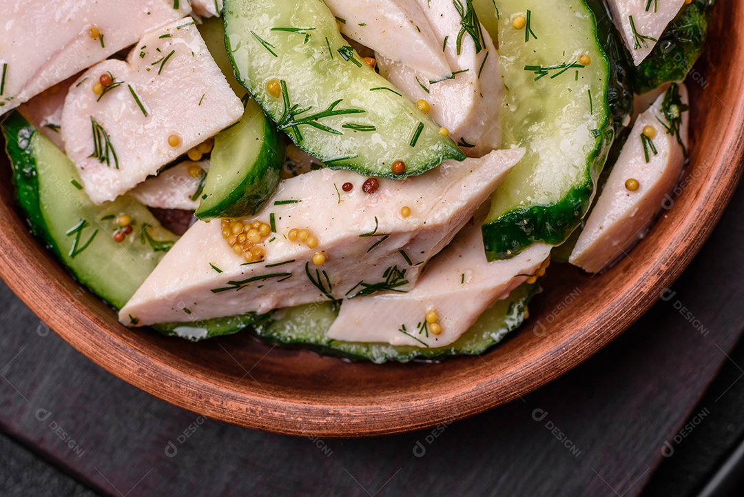 Deliciosa salada fresca e suculenta de pepino e fatias de frango grelhado, com mostarda francesa, sal e especiarias sobre um fundo escuro de concreto