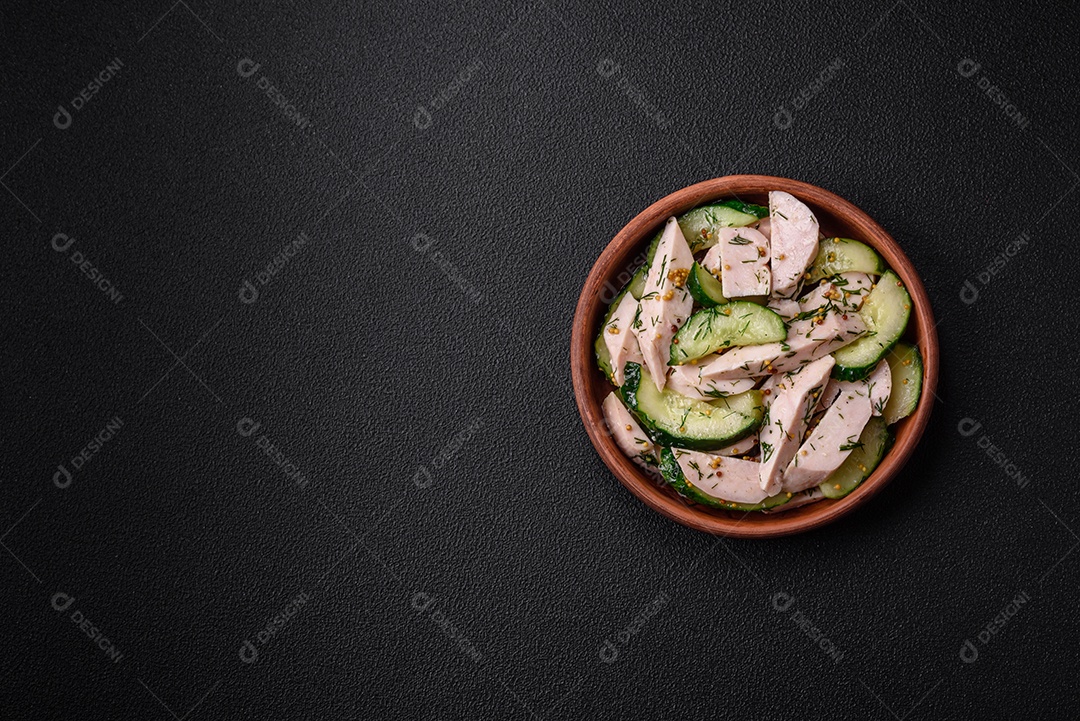 Deliciosa salada fresca e suculenta de pepino e fatias de frango grelhado, com mostarda francesa, sal e especiarias sobre um fundo escuro de concreto