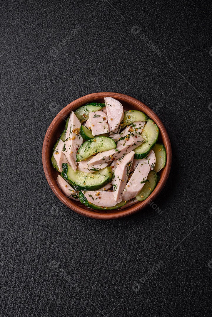 Deliciosa salada fresca e suculenta de pepino e fatias de frango grelhado, com mostarda francesa, sal e especiarias sobre um fundo escuro de concreto