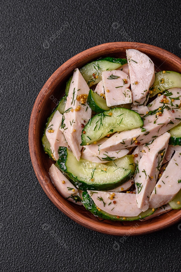 Deliciosa salada fresca e suculenta de pepino e fatias de frango grelhado, com mostarda francesa, sal e especiarias sobre um fundo escuro de concreto