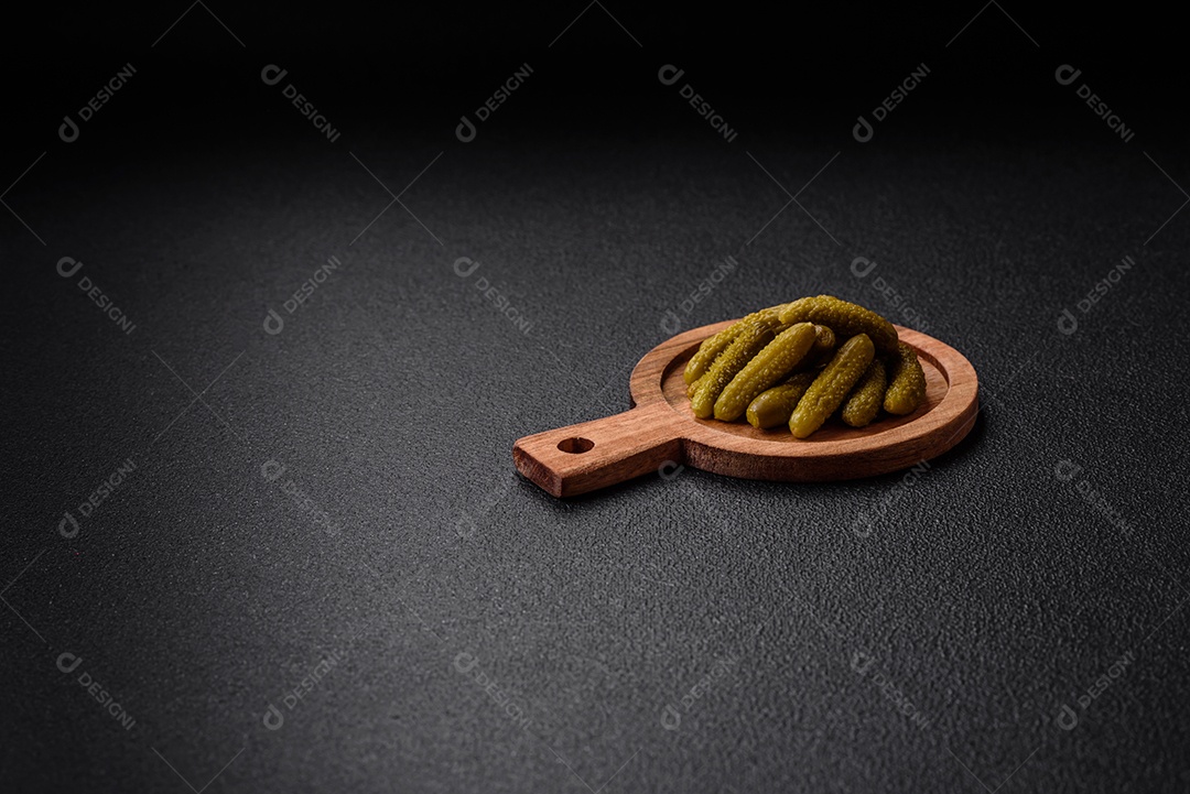 Deliciosos pequenos pepinos em conserva com cebola, mostarda, sal e especiarias sobre um fundo escuro de concreto