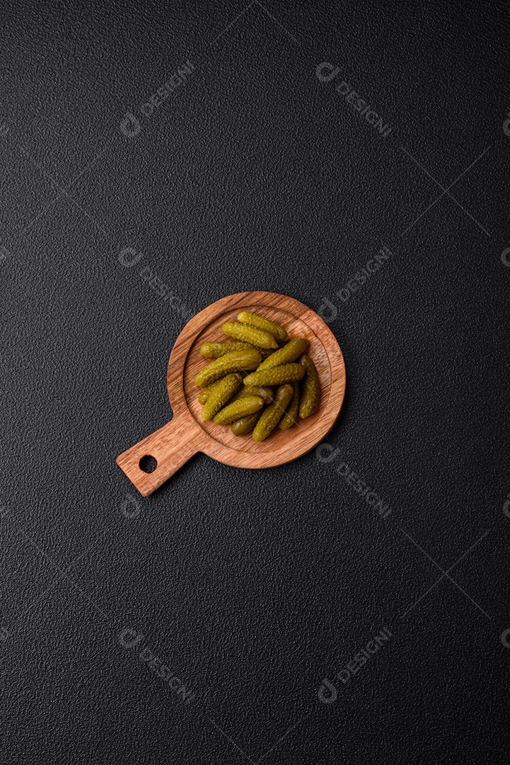 Deliciosos pequenos pepinos em conserva com cebola, mostarda, sal e especiarias sobre um fundo escuro de concreto