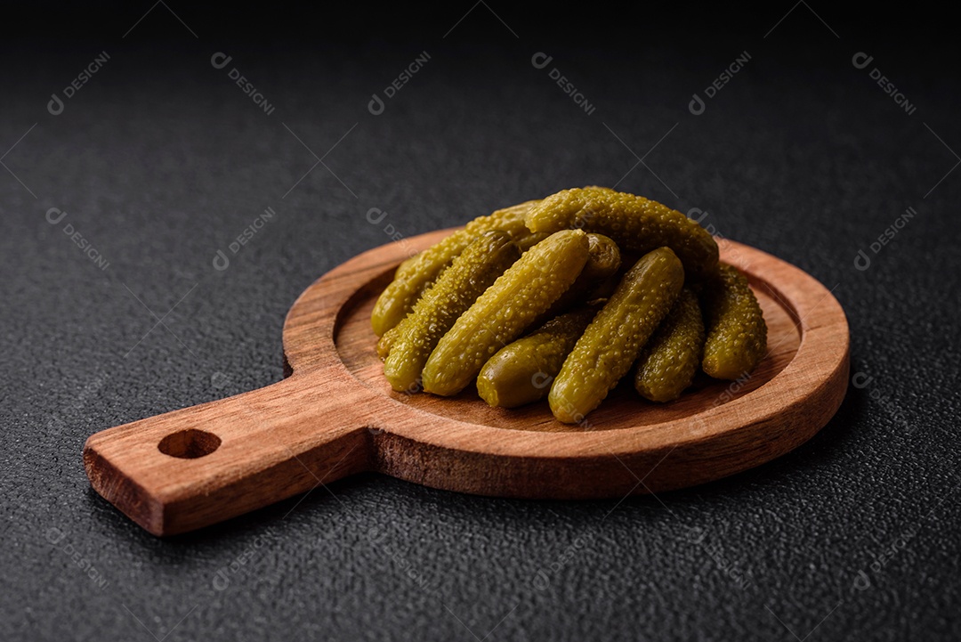 Deliciosos pequenos pepinos em conserva com cebola, mostarda, sal e especiarias sobre um fundo escuro de concreto