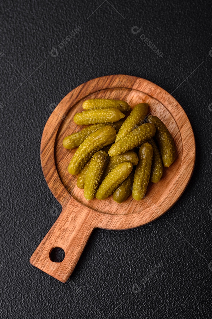 Deliciosos pequenos pepinos em conserva com cebola, mostarda, sal e especiarias sobre um fundo escuro de concreto