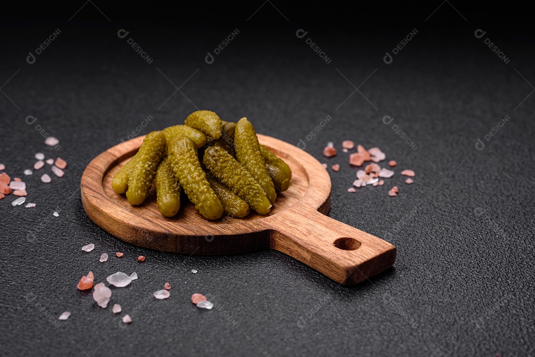 Deliciosos pequenos pepinos em conserva com cebola, mostarda, sal e especiarias sobre um fundo escuro de concreto