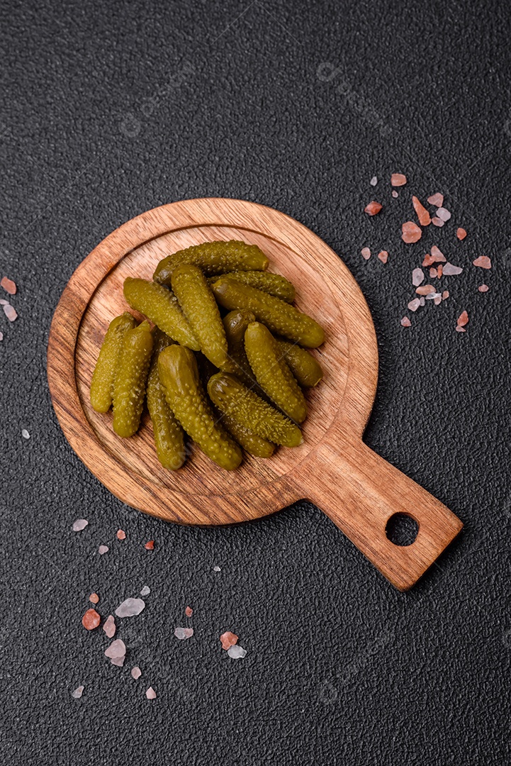 Deliciosos pequenos pepinos em conserva com cebola, mostarda, sal e especiarias sobre um fundo escuro de concreto